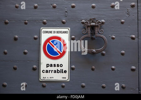 Old metal doorknocker and No Parking sign on the black painted wooden gate fixed with rivets in Bergamo, Lombardy, Italy. Stock Photo