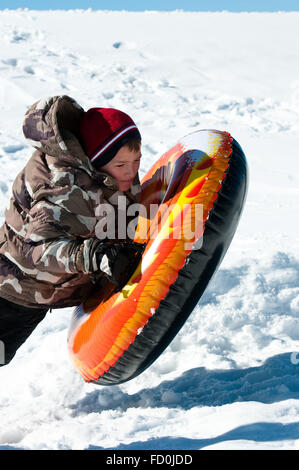 Young teenage boy riding on a colorful tube down a snowy hill. Stock Photo