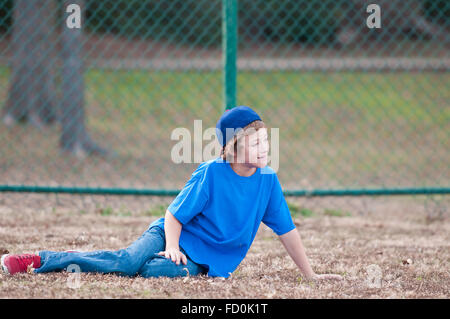 Young baseball boy in blue denim with red shoes laying in the grass at a ballpark. Stock Photo