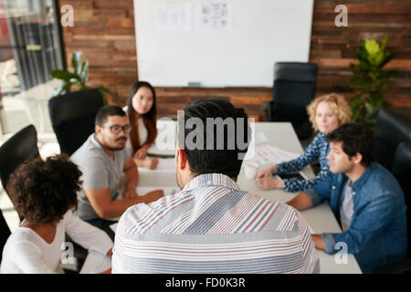 Rear view portrait of man explaining business plan to coworkers during a meeting in conference room.  Young people meeting in bo Stock Photo