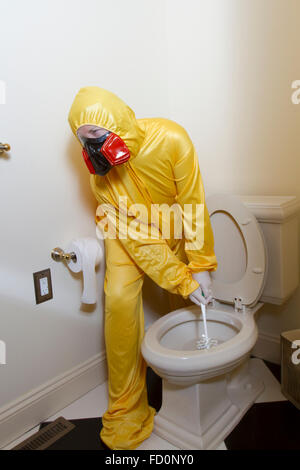 Woman dressed in yellow haz mat uniform and ventilator cleaning the bathroom toilet with scrub brush. Stock Photo