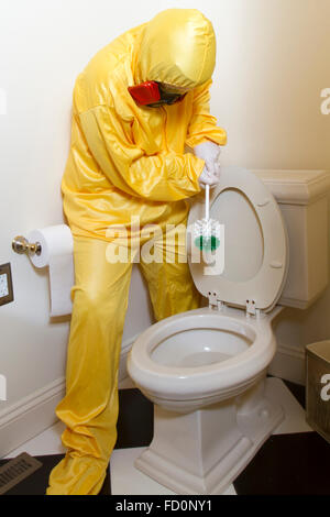 Woman dressed in yellow haz mat uniform and ventilator cleaning the bathroom toilet with scrub brush. Stock Photo