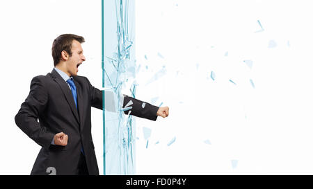 Young determined businessman breaking glass with karate punch Stock Photo