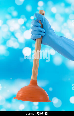 Toilet plunger in gloved hand on blue background for drainage, r Stock Photo