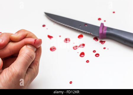 Hand, knife and drops of blood on a white surface