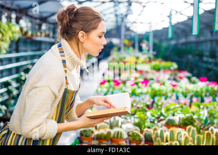Profile of serious pretty young woman with book working in garden center Stock Photo
