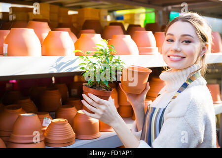 Happy lovely young woman gardener buying new pot for her plant in the shop Stock Photo