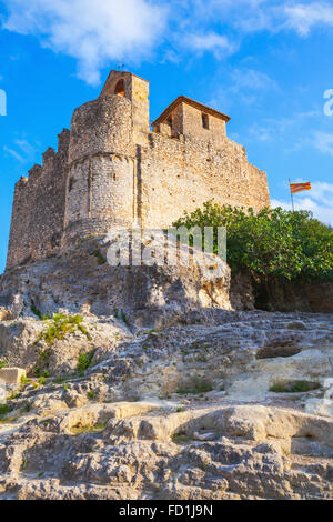 Medieval stone castle and flag of Catalonia on the rock in Spain. Main landmark of Calafell town, vertical photo Stock Photo