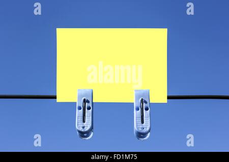 Blank yellow sticky note with blue clippers on blue sky background Stock Photo