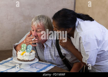 Naughty old pensioner lighting his cigarette on his birthday cake Stock Photo