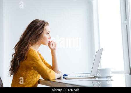Portrait of a thoughtful woman sitting at the table with laptop computer at home Stock Photo