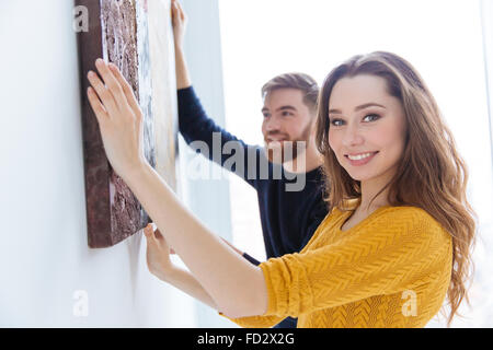 Cheerful couple hanging picture on the wall at home Stock Photo