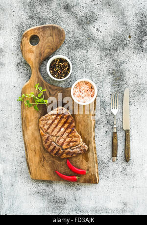 Grilled ribeye beef steak with herbs and spices on walnut cutting board over grunge greyn background, top view Stock Photo
