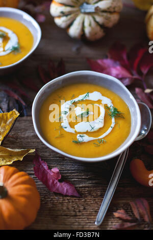 Pumpkin and sweet potatoes soup in bowls topped with cream and fresh dill, Autumn leaves on a rustic wooden table Stock Photo