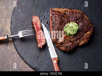 Medium rare grilled Black Angus Steak Ribeye with herb butter on fork on stone slate plate Stock Photo