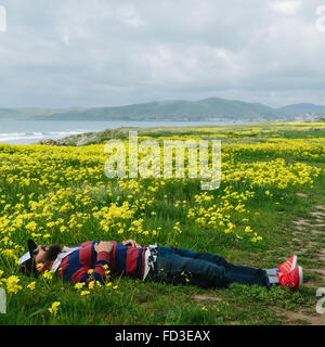 A man rests in a field of yellow flowers on the shoreline of Big Sur, California. Stock Photo