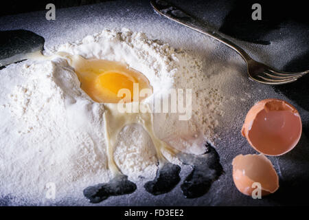 Ingredients for dough making. Sifted flour and brocken egg on black slate board. Stock Photo