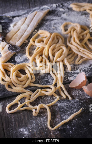 Making homemade pasta pici. Sliced rolled dough for pasta and prepared long pasta on black slate board with flour and egg shell Stock Photo