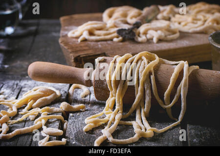 Fresh homemade pici pasta on wood chopping board over old wooden table with flour and rolling-pin. Dark rustic style. See proces Stock Photo