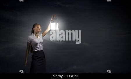 Young businesswoman walking in darkness with lantern in hand Stock Photo