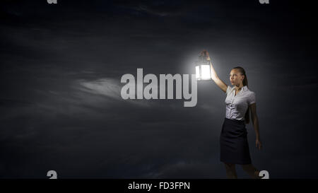 Young businesswoman walking in darkness with lantern in hand Stock Photo