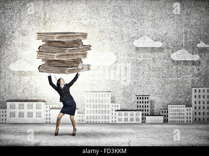 Young businesswoman in paper crown lifting books above head Stock Photo