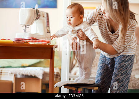 Mother and infant, home, the baby first steps, natural light. Child care combined with work at home. Stock Photo