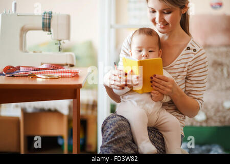 Mother and baby reading a book together at home. Stock Photo