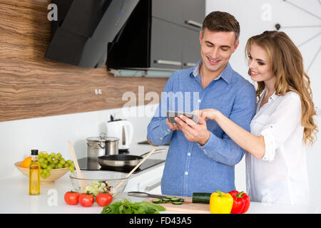 Beautiful couple using smartphone and cooking on the kitchen at home Stock Photo
