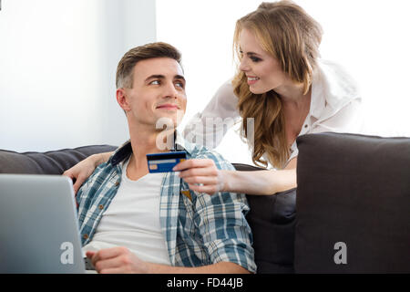 Happy couple making purchases in the internet using laptop and  credit card sitting on sofa in living room Stock Photo