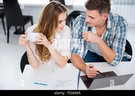 Happy colleagues sitting in office and working with laptop together Stock Photo
