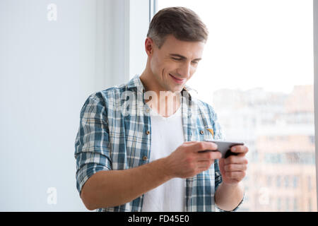 Handsome smiling male using smartphone standing near the window Stock Photo