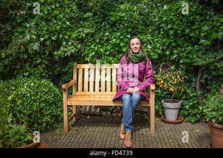 Beautiful young woman sits on the bench after the rain and enjoying the sun came out in a summer garden Stock Photo