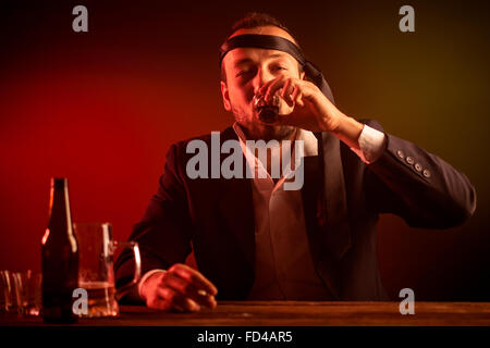 Drunk Businessman with a Neck Tie around His Head Drinking a Shot in a Pub Stock Photo