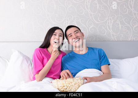 Young couple watching popcorn movie in bed Stock Photo