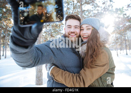 Happy young couple making photo on smartphone in winter park Stock Photo