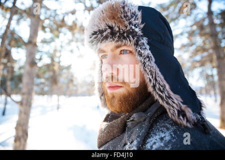 Closeup portrait of attractive thoughtful bearded young man in winter hat standing outdoors Stock Photo