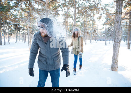 Joyful pretty young woman thowing snowballs in handsome happy young man in winter park Stock Photo