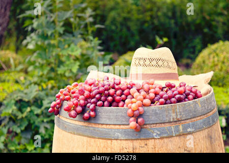 Freshly picked red grapes and a straw hat on wooden barrel. Stock Photo