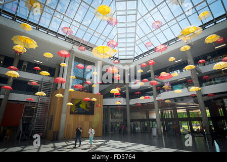 Two people walk under suspended yellow and red parasols made from lace in the cultural center Bonlieu in Annecy Stock Photo