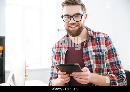 Happy handsome bearded male in glasses using tablet in the office Stock Photo