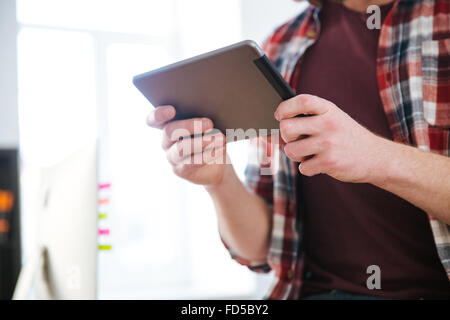 Closeup of tablet used by man in checkered shirt standing in the office Stock Photo