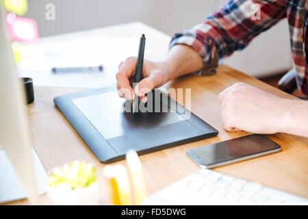 Closeup of black pen tablet with stylus used by male designer hand on wooden table Stock Photo