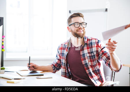 Happy handsome bearded designer using graphic pen tablet with stylus and receiving blueprints Stock Photo