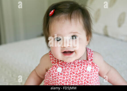 Precious, wide-eyed baby girl staring at the camera smiling. Stock Photo