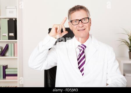 Middle-aged male doctor working in his office having a brainwave or breakthrough idea as he raises his finger with a happy smile Stock Photo