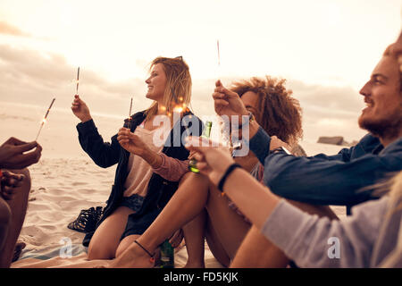 Group of friends having fun with sparklers outdoors at the beach. Diverse group of young people celebrating new year's day at th