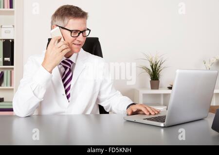 Medical Doctor Talking to Client Using Phone While Reading at Laptop Stock Photo