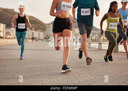 Diverse group of runners competing in a race. Athletes sprinting on a street along the sea. Stock Photo