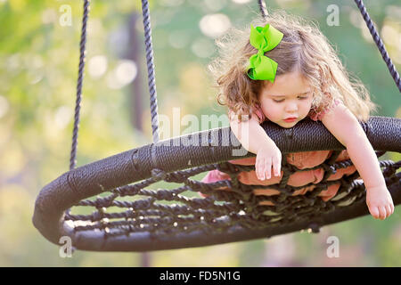 Toddler girl laying on her stomach on a swing as if pretending to fly. Stock Photo